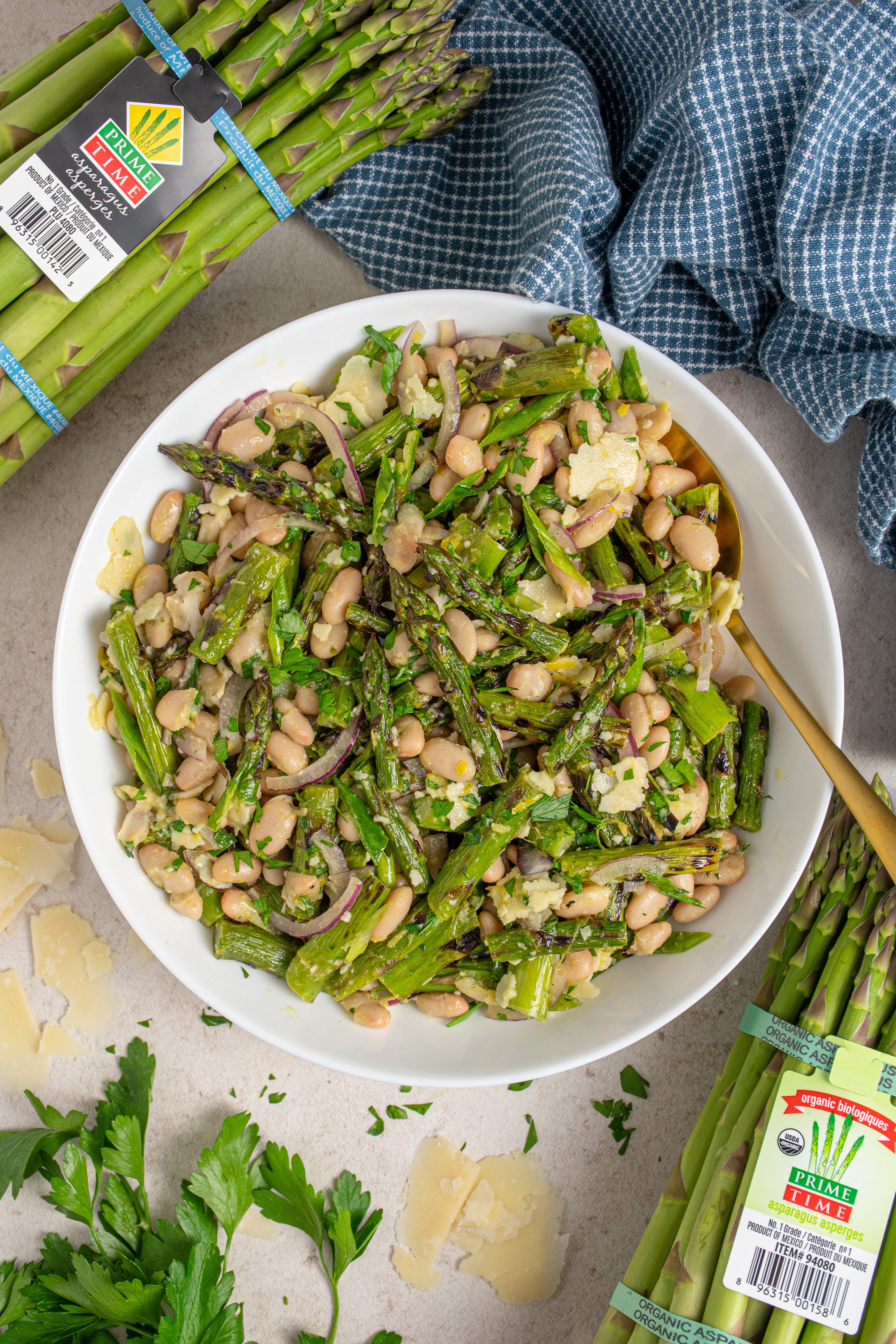White bean and asparagus salad in a white bowl with fresh asparagus on the side.