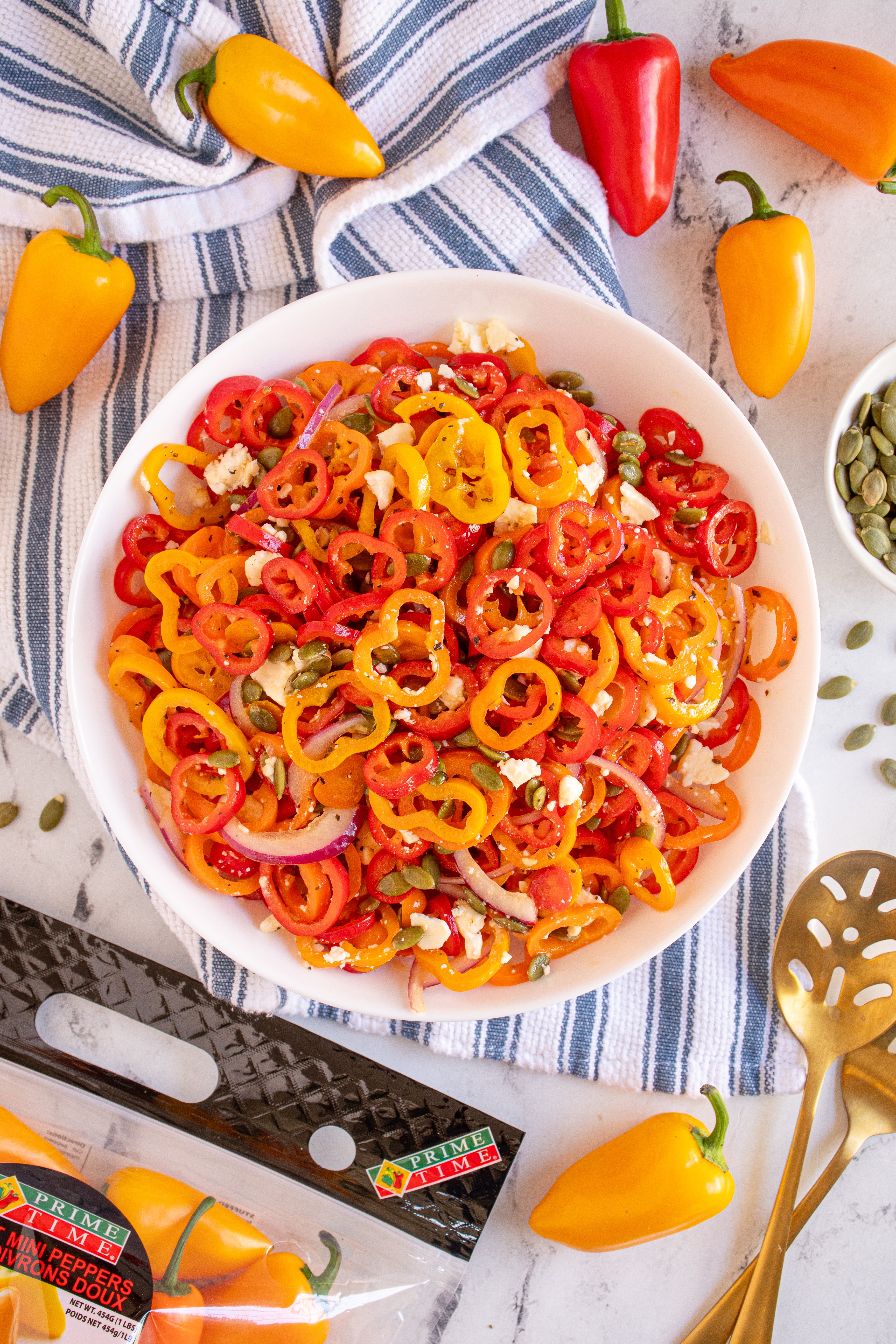 Colorful bell pepper salad in a white bowl with fresh peppers around on a marble surface.